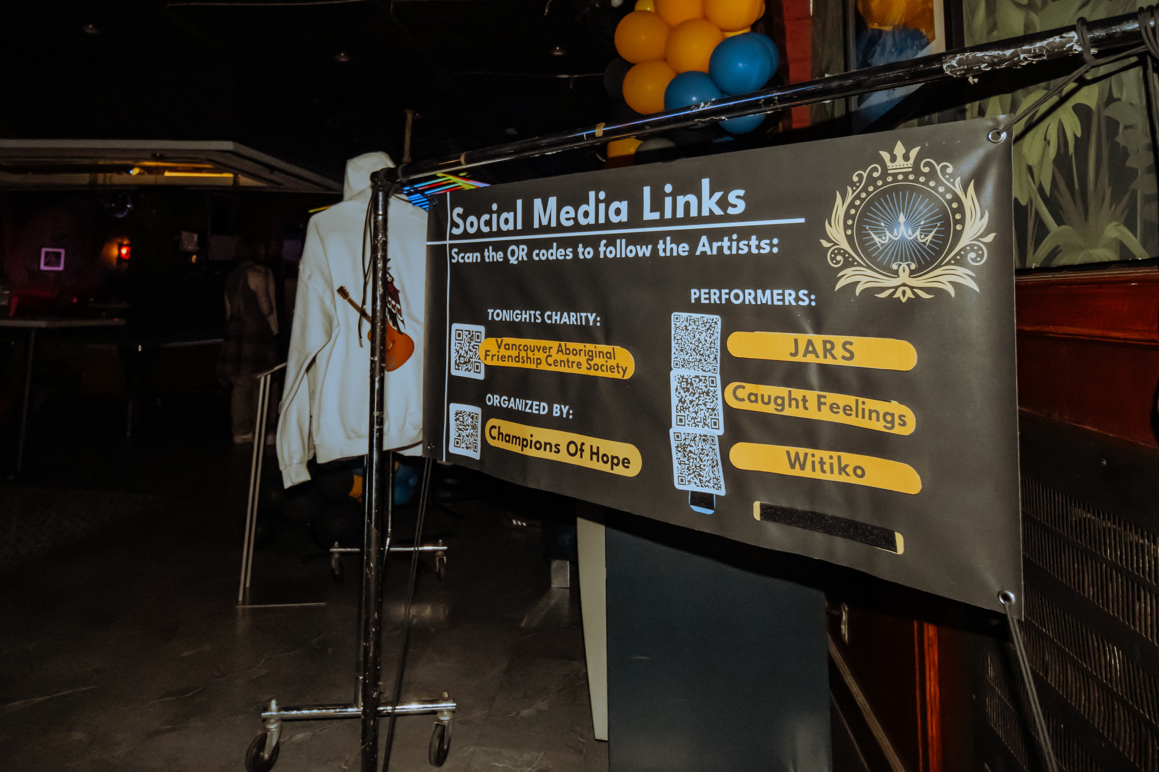 Social media links banner with artist and charity QR codes at a Champions of Hope event